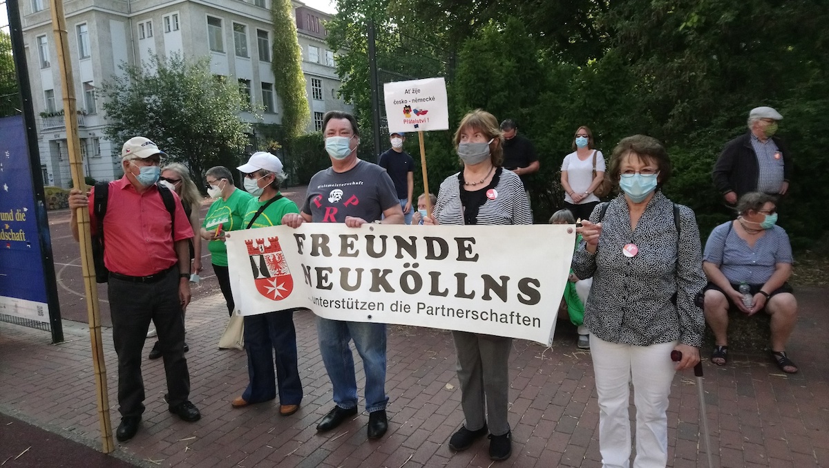 Drei Troedler*innen im Vordergrund mit Mundschutz halten zusammen ein Banner des Vereins "Freunde Neuköllns" vor sich