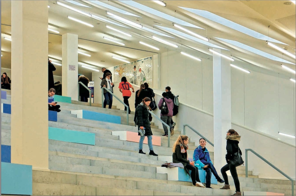 Große, breite und helle Treppe mit eingebauten Sitzbänken und Schueler:innen der Sekundarstufe