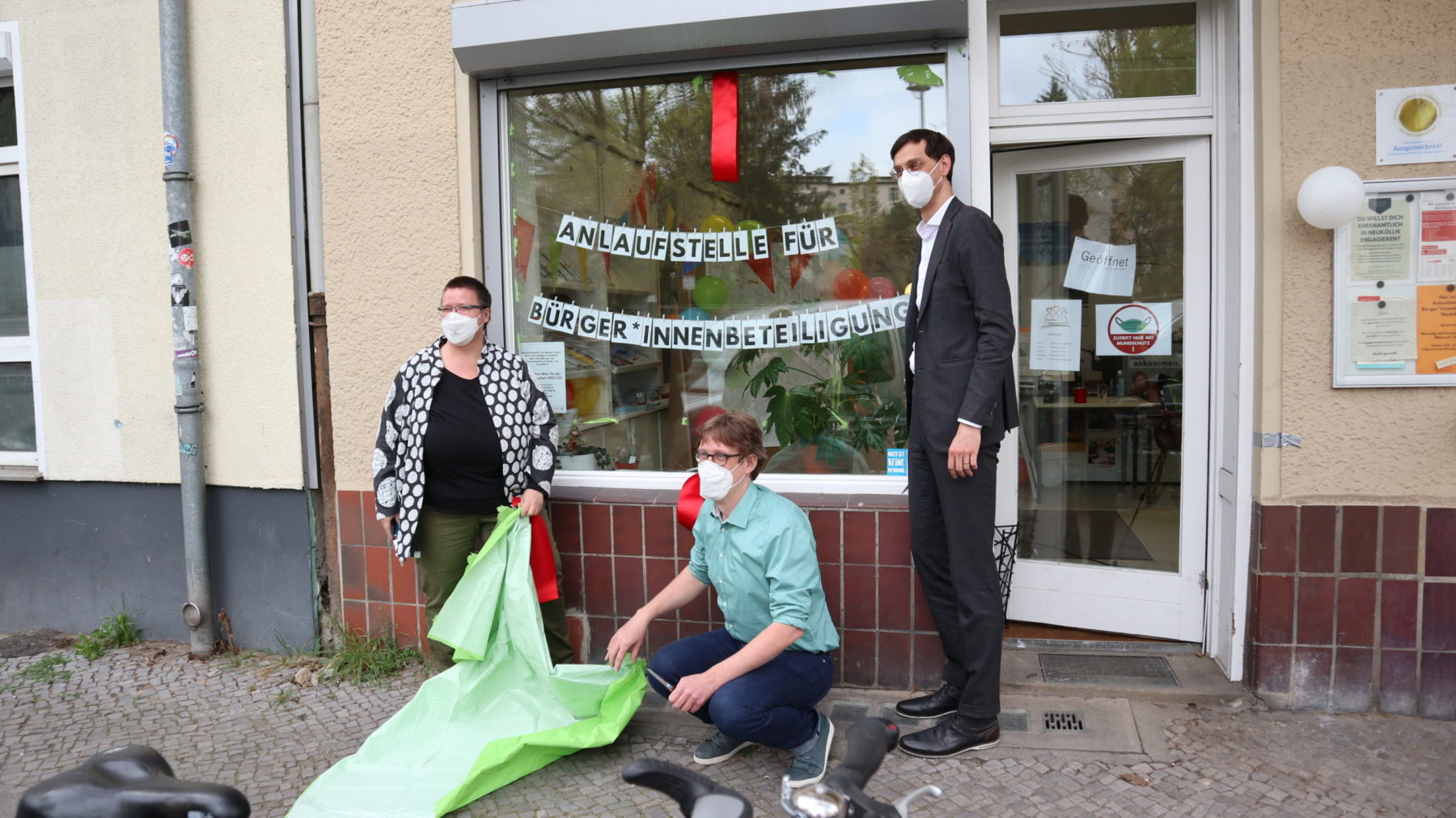 Vor dem Schaufenster des NEZ stehen von links nach rechts Gisela Enders, Juochen Biedermann (hockend) und Martin Hikel