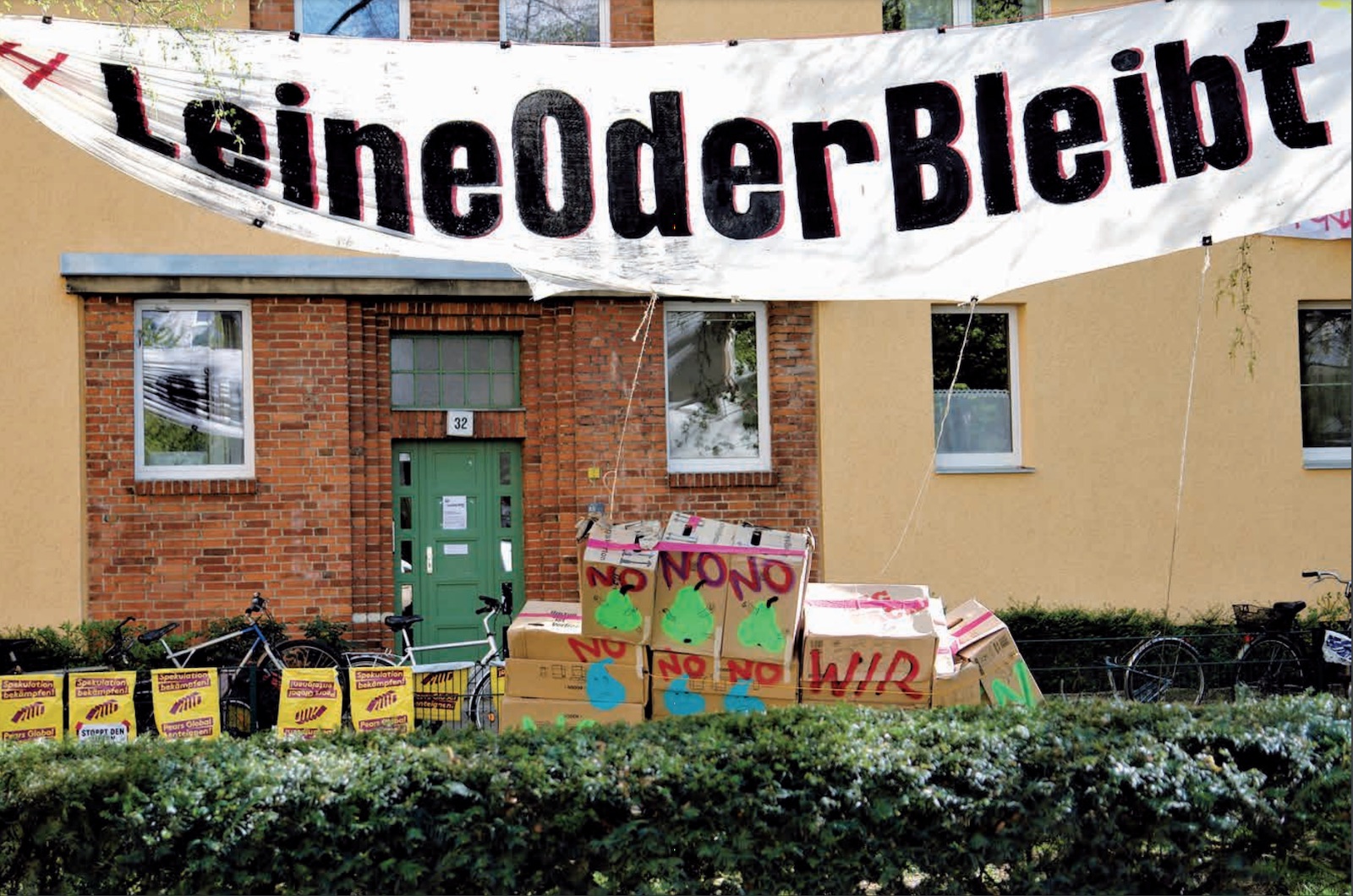 Banner mit "LeineOder Bleibt" hängt vor einem Haus, vor dem Haus stehen gestapelte Pappkartons mit der Aufschrift "No"