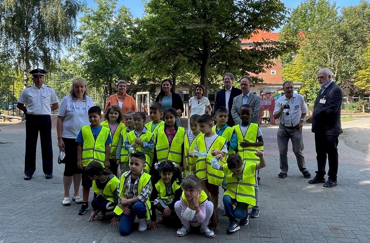 Eine Gruppe Grundschulkinder schaut in die Kamera. 3 hocken vorn, 12 stehen dahinter. Sie tragen gelbe Warnwesten. Hinter den Kindern stehen Frauen und Männer und schauen in das Bild.