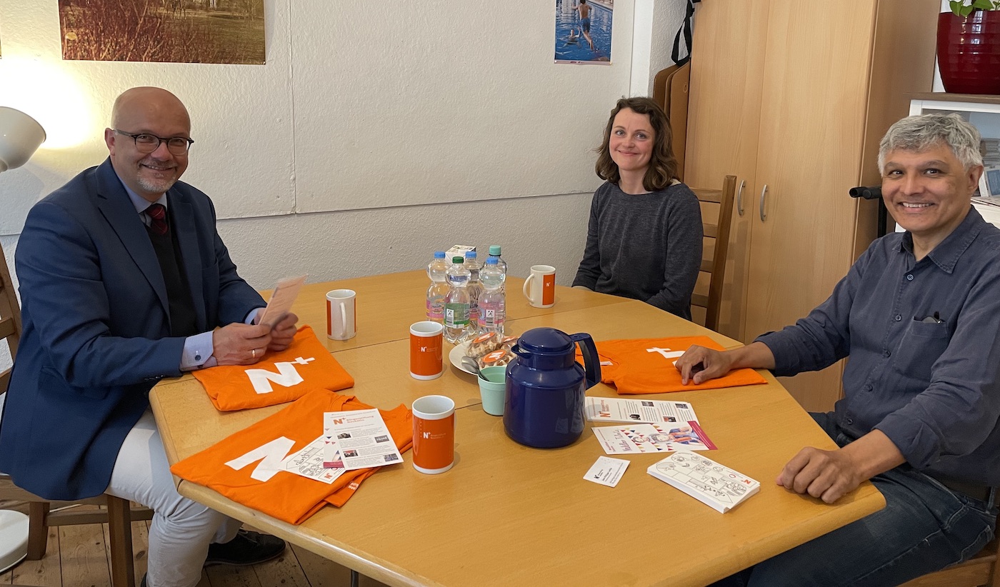 Fritz Felgentreu, Simone Rajilic und Jean-Philippe Laville (v.l.nr.)sitzen mit Abstand am runden Tisch unseres N+Büros. Auf dem Tisch stehen Tassen und eine Kanne, liegen N+T-Shirts, Prospekte