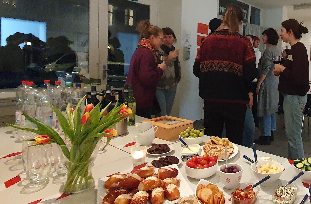 Buffettisch mit Tulpenstrauß im Vordergrund, im Hintergrund unterhüält sich eine Gruppe von Menschen