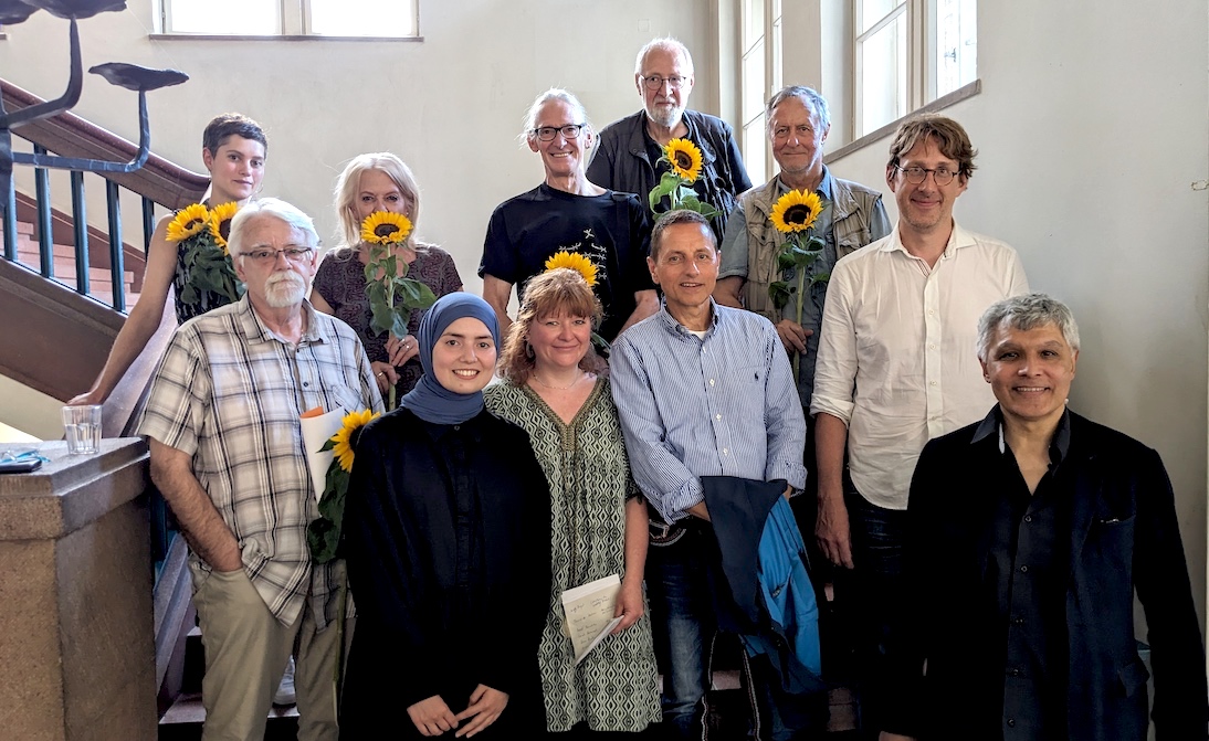 Elf Menschen stehen auf einer Treppe und lächeln in die Kamera. Einige halten Sonnenblumen in der Hand.