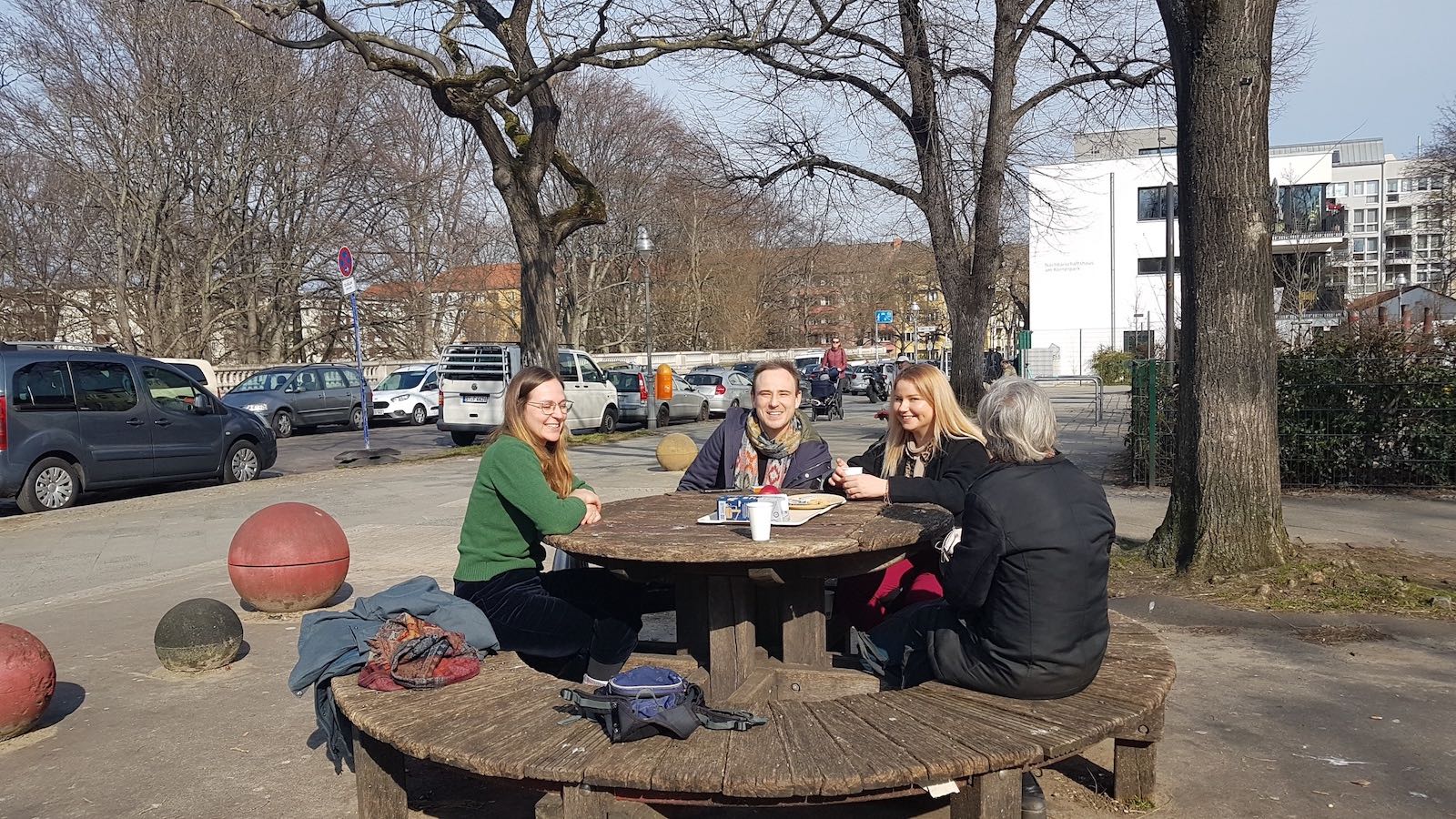 2 Personen sitzen um einen runden Holztisch im Freien.